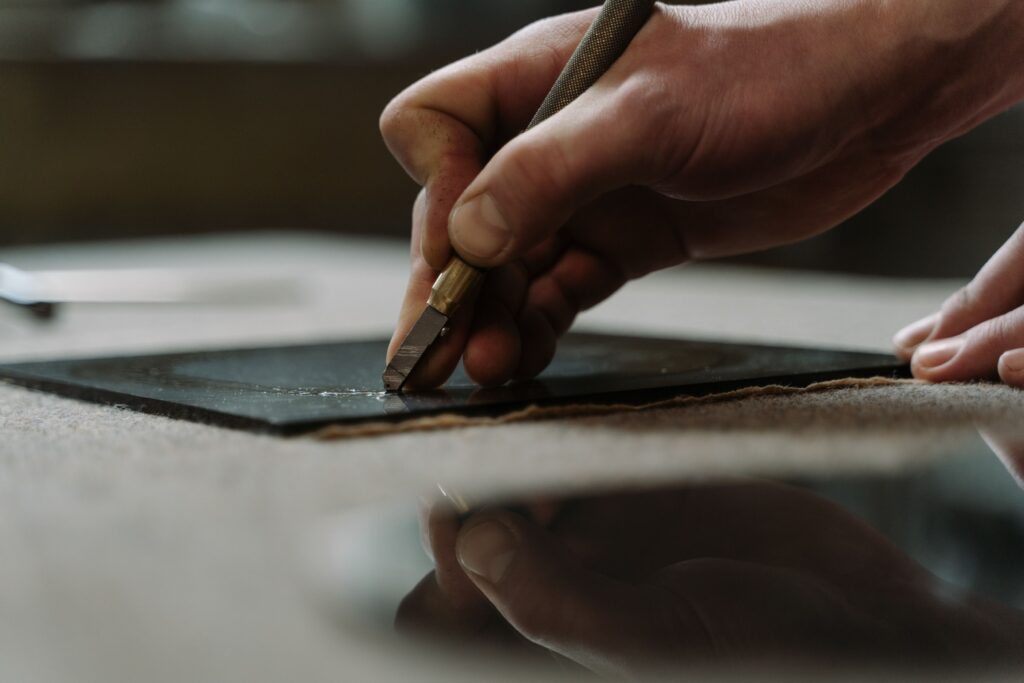 Detailed view of a hand skillfully using a glass cutter on a black surface in an indoor workspace.